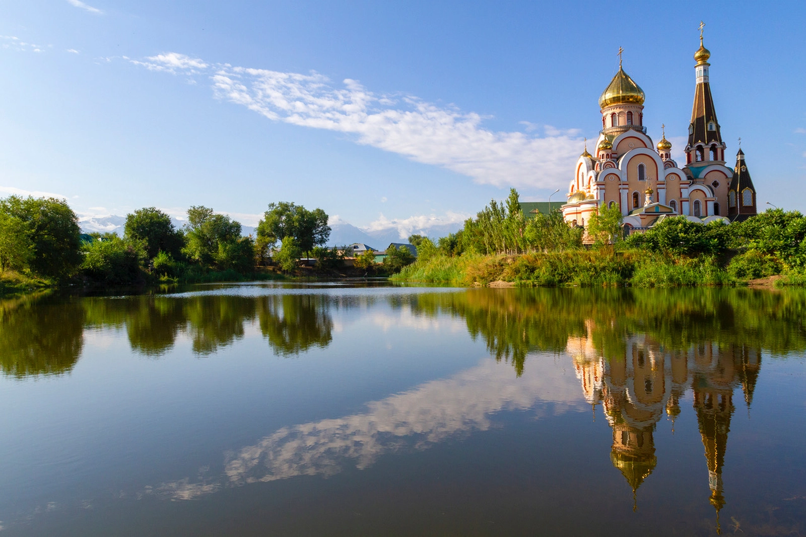 Golden-domed Orthodox church reflected in a calm lake surrounded by greenery